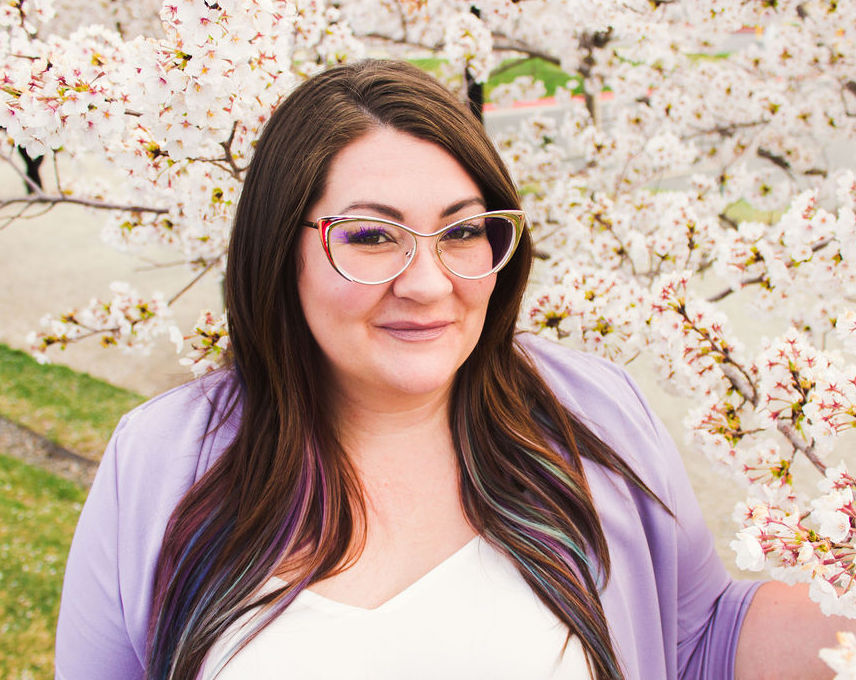 Melanee Dahl smiles at the camera surrounded by white cherry blossoms.